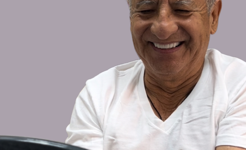 A man in a white t-shirt, smiling as he looks at his new dental implants in a mirror.