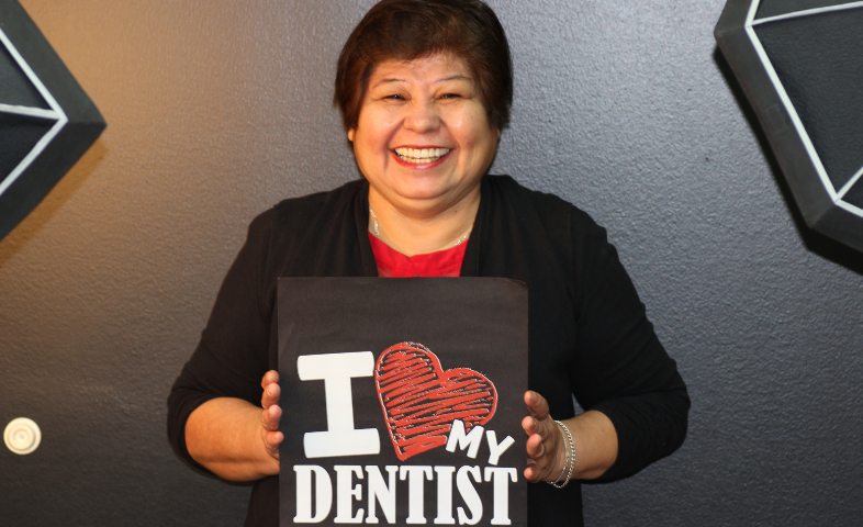 A patient with a wide, happy smile holding a sign that says "I love the dentist".
