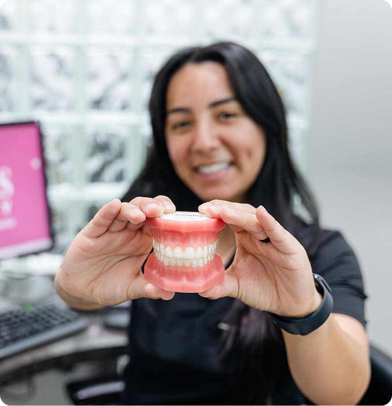 Dental professional smiling and holding a model of human teeth in a clinic.